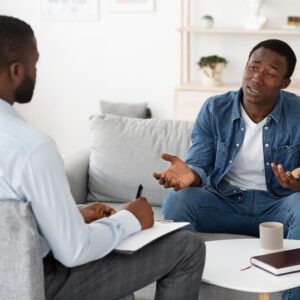 Stressed black man explaining his problems to psychologist at individual therapy session at office, copy space