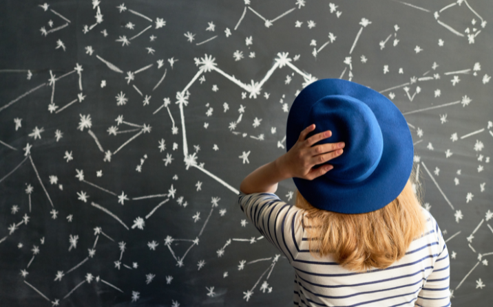Rear view of female astrologer looking at blackboard with pictured constellation of stars in shape of heart